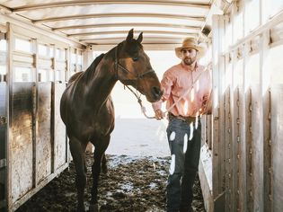Man loading horse into stall in trailer